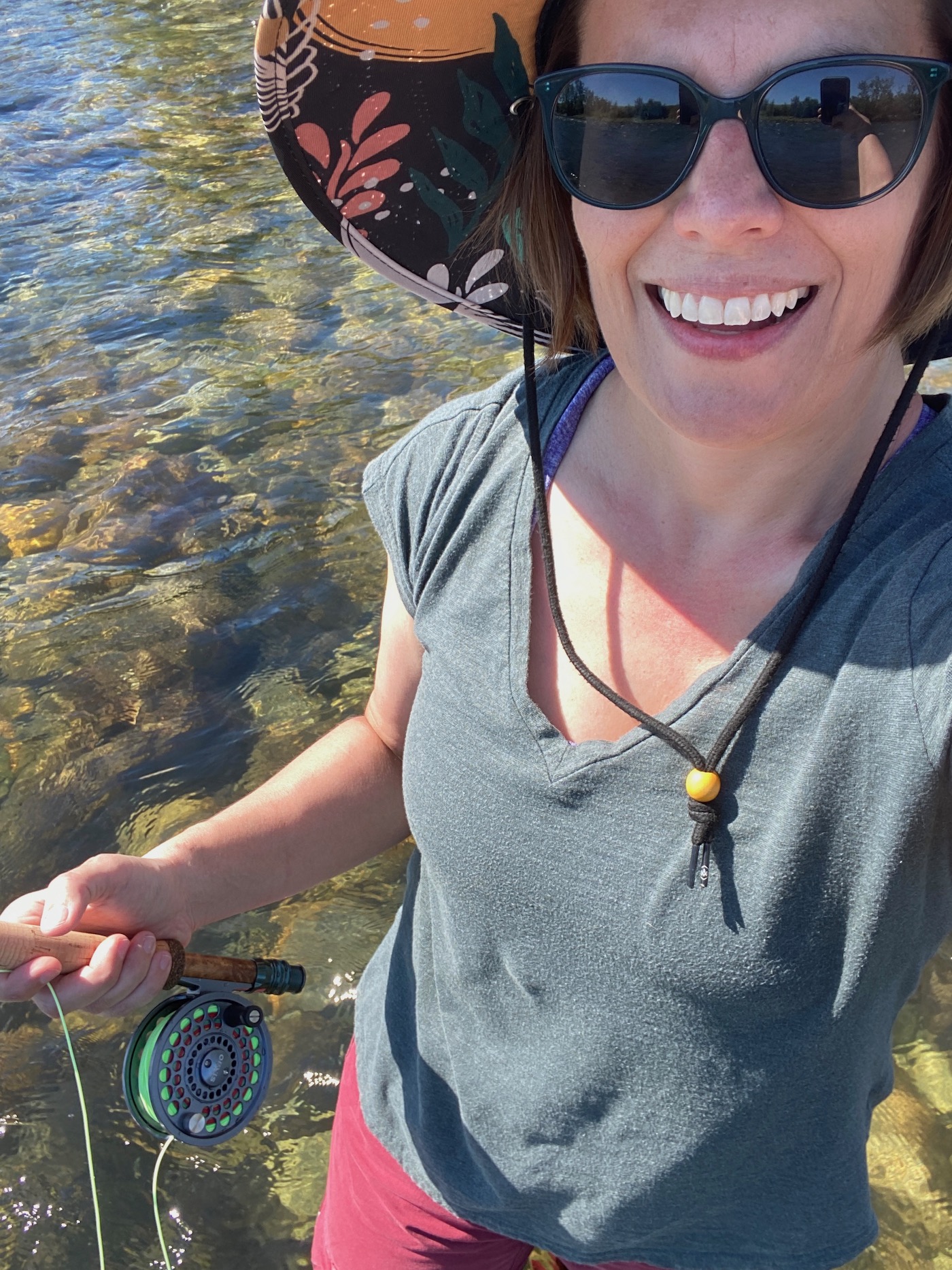 Girl wearing sunglasses and a hat fly fishing on the Spokane River