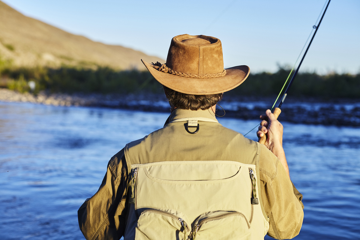 Man-wearing-a-vest-and-hat-while-fly-fishing-on-a-river
