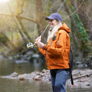 Woman-fly-fishing-on-a-river-in-a-soft-shell-orange-jacket