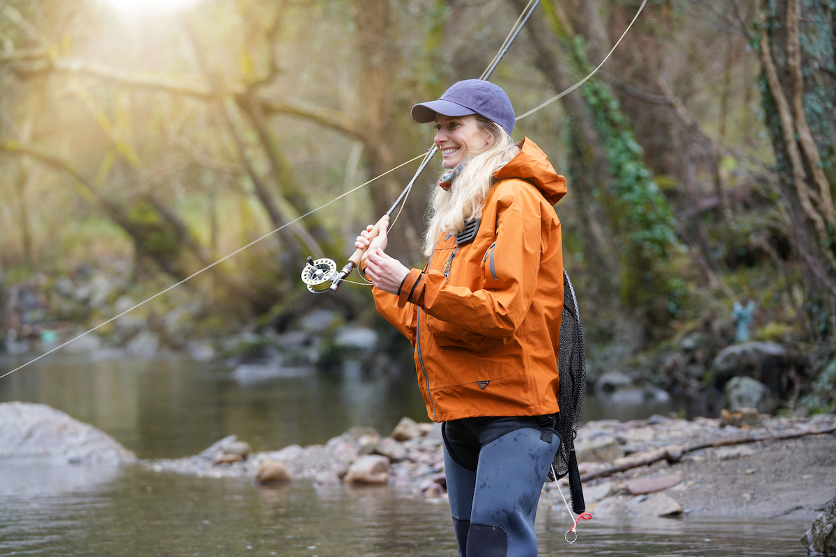 Woman-fly-fishing-on-a-river-in-a-soft-shell-orange-jacket