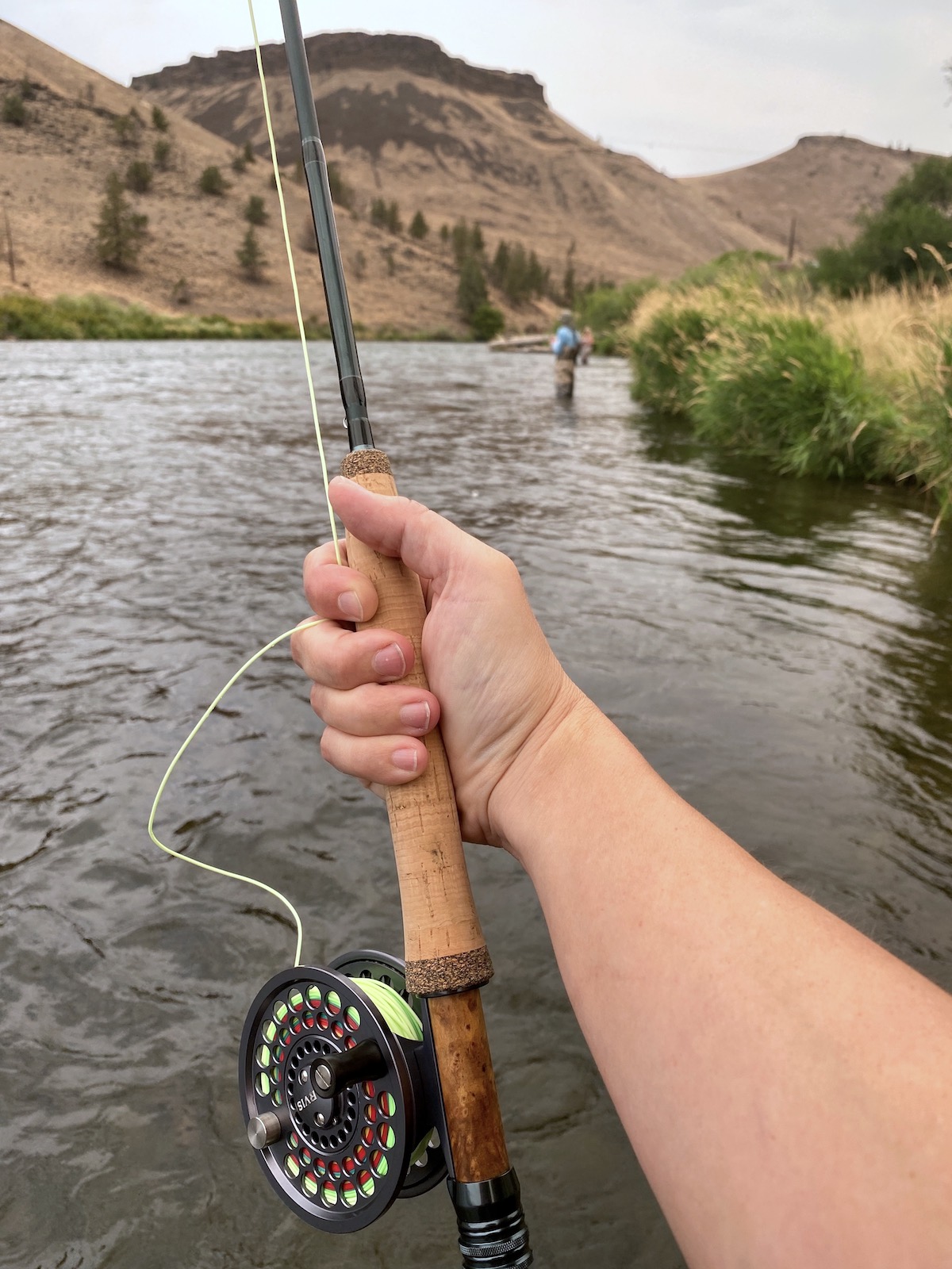 Hand holding a fishing rod and reel out over a river